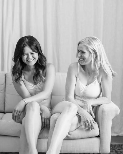 Two women sitting on a couch, smiling and laughing together.